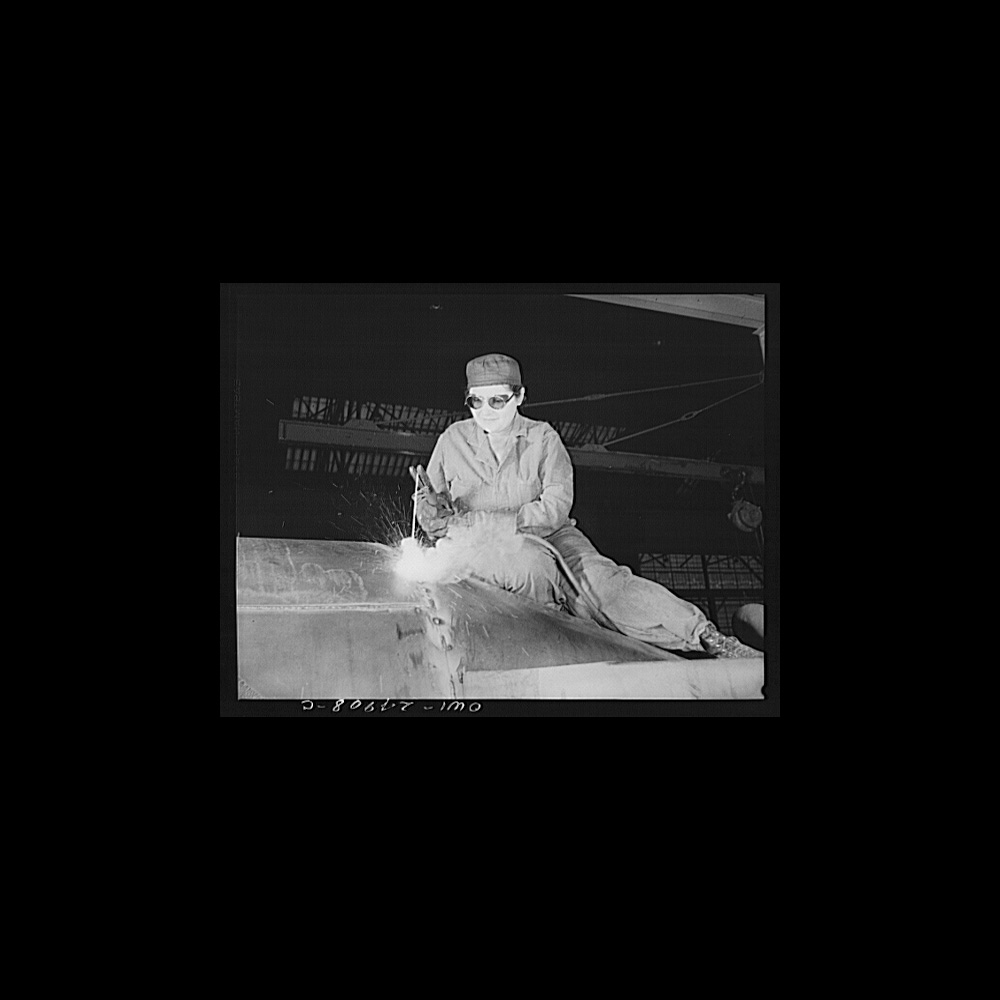 Black and white photograph of Enola O’Connel wearing coveralls, a cap and welders goggles working atop a gasoline trailer for the U.S. Army Air Corps, 1943. She was the only woman welder in the Heil Company’s plant.] 