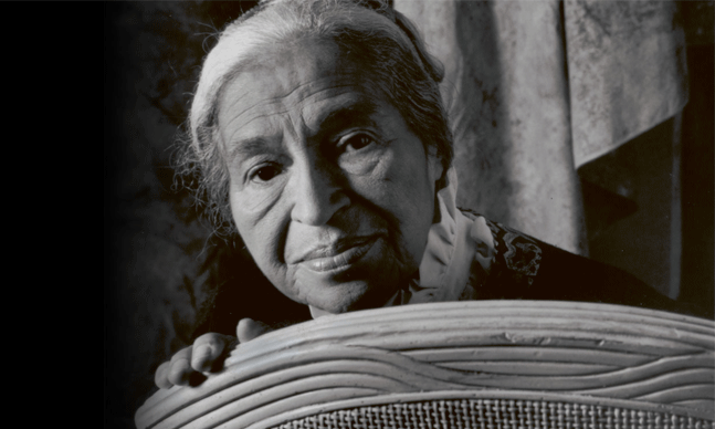 Black and white photograph of Rosa Parks looking over the back of a chair.